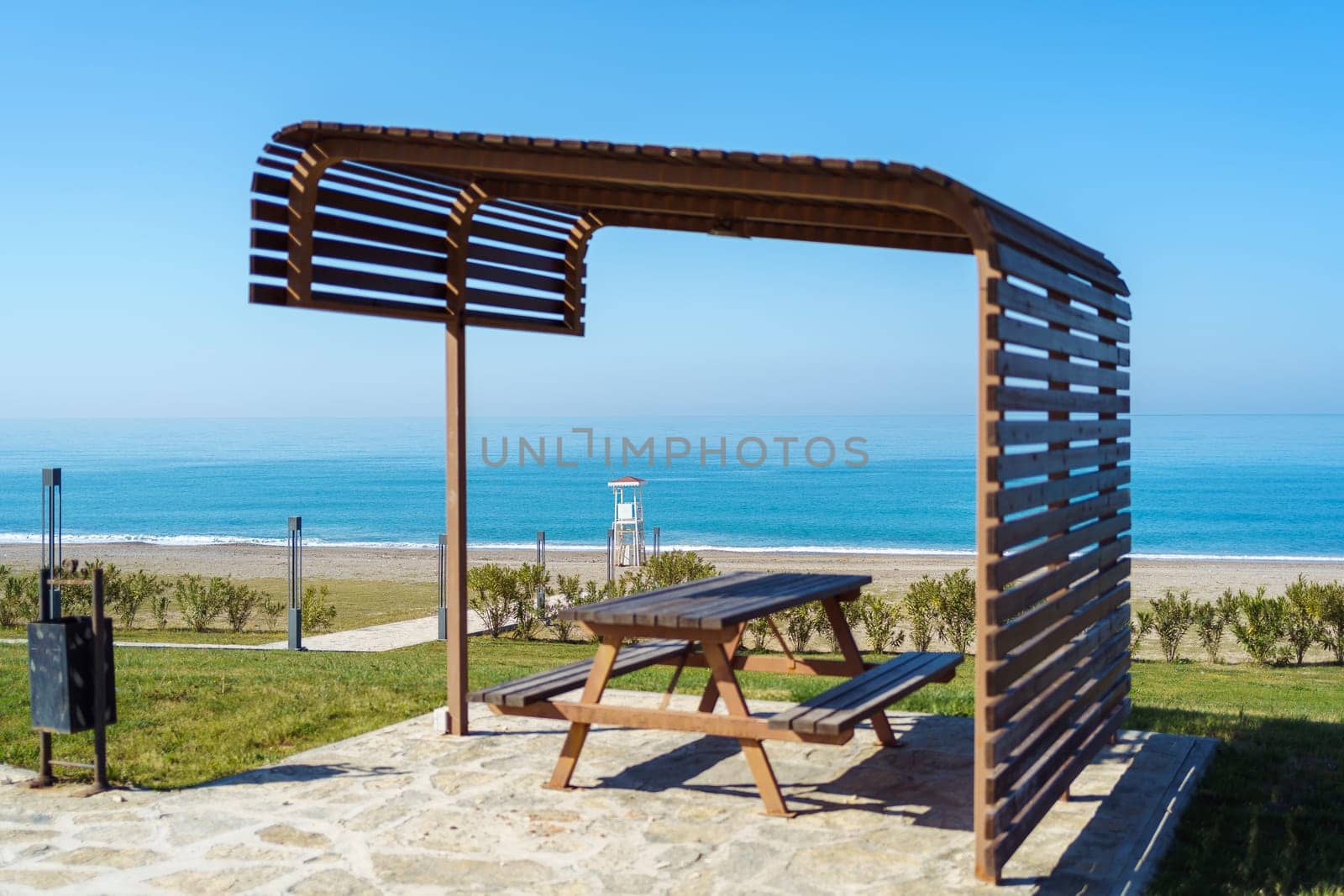 Scenic view of empty rest area near sandy shore beach ocean sea. Landscape of rest place picnic equipment camper site wooden dinner table and benches standing by the seashore shoreline