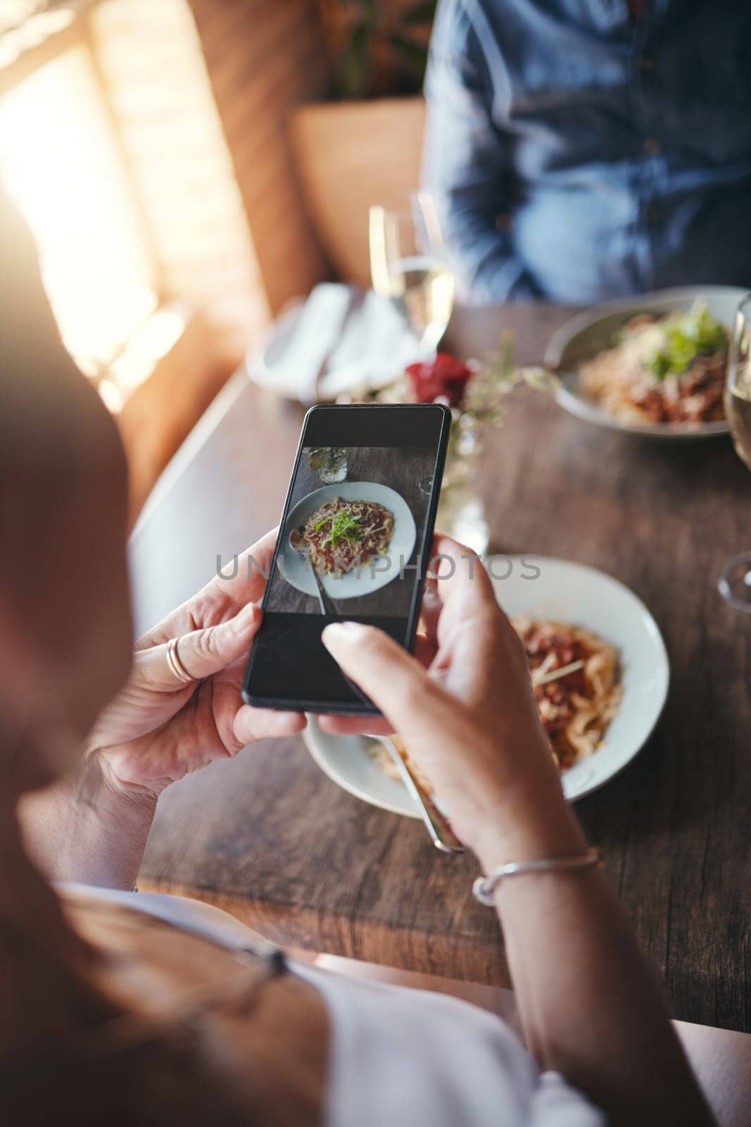 Phone, food and social media with the hands of a woman taking a photograph while eating in a restaurant during a date. Mobile, internet and romance with a female snapping a picture while dating by YuriArcurs