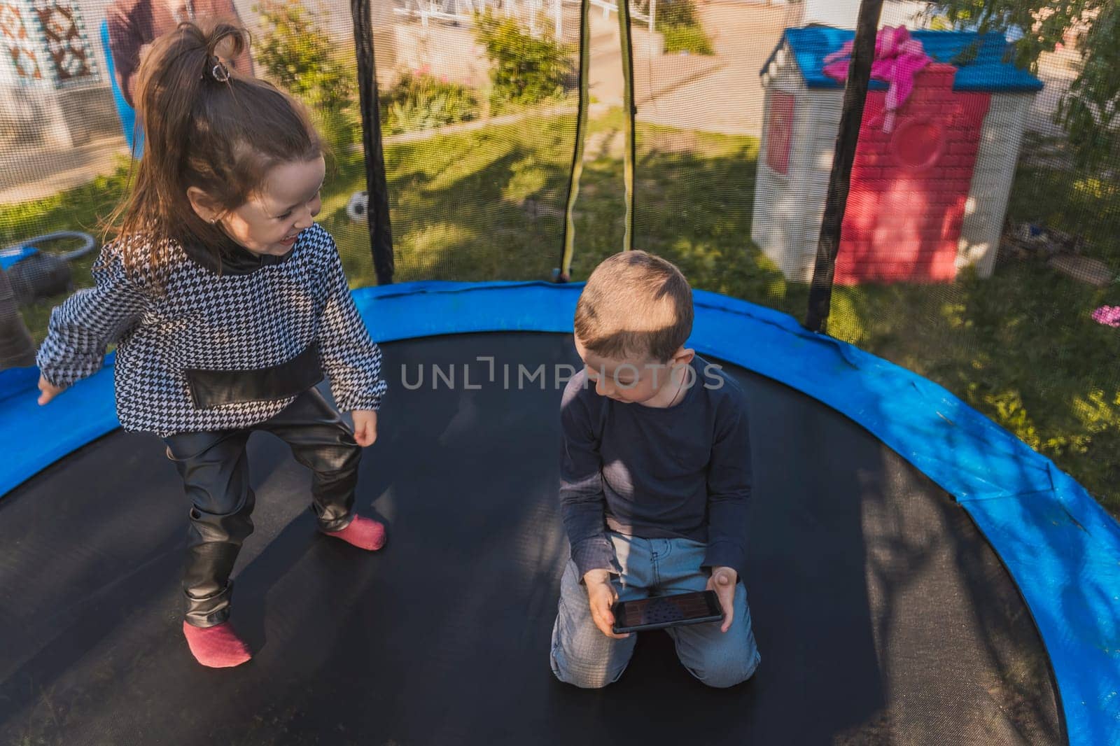 portrait of children who sit on a trampoline and look at the phone