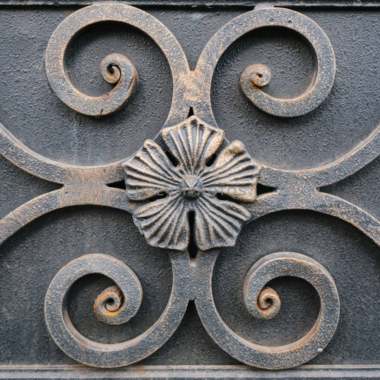 Floral pattern forged ornament of rough grey metal surface closeup. Metallic flowers on steel texture. Old iron panel with primitive floral pattern. Vintage carved iron relievo backdrop.