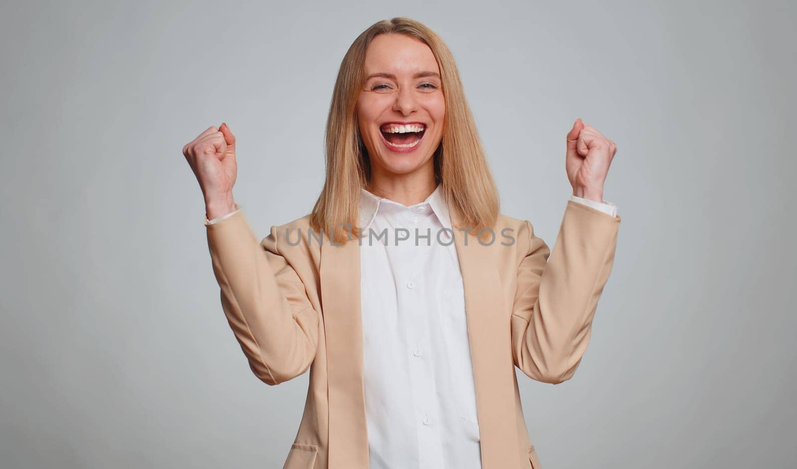 Happy joyful office business woman shouting, raising fists in gesture I did it, celebrating success, winning, birthday, lottery jackpot goal achievemen, good news. Adult girl on gray studio background