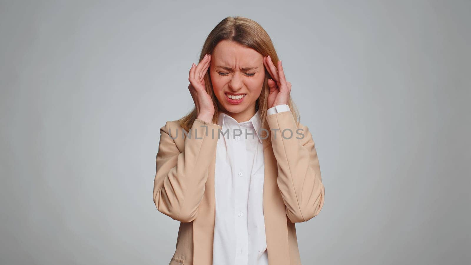 Business woman in formal office suit rubbing temples to cure headache problem, suffering from tension, migaine, stress, grimacing in pain, high blood pressure isolated alone on gray wall background