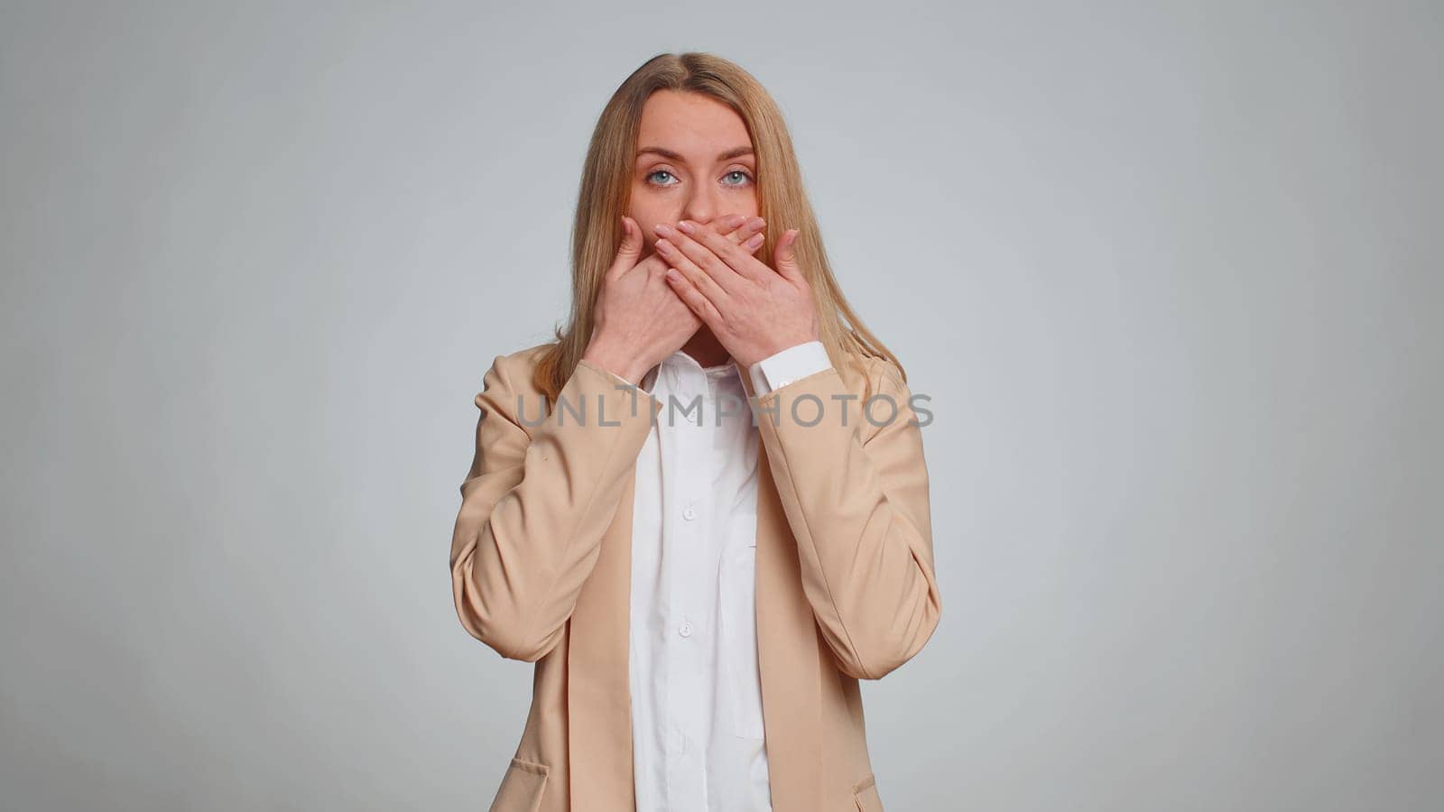 I will not say anyone any word. Frightened woman closing mouth with hands looking intimidated scared at camera gestures no refusing to tell terrible secret, unbelievable truth. Girl on gray background