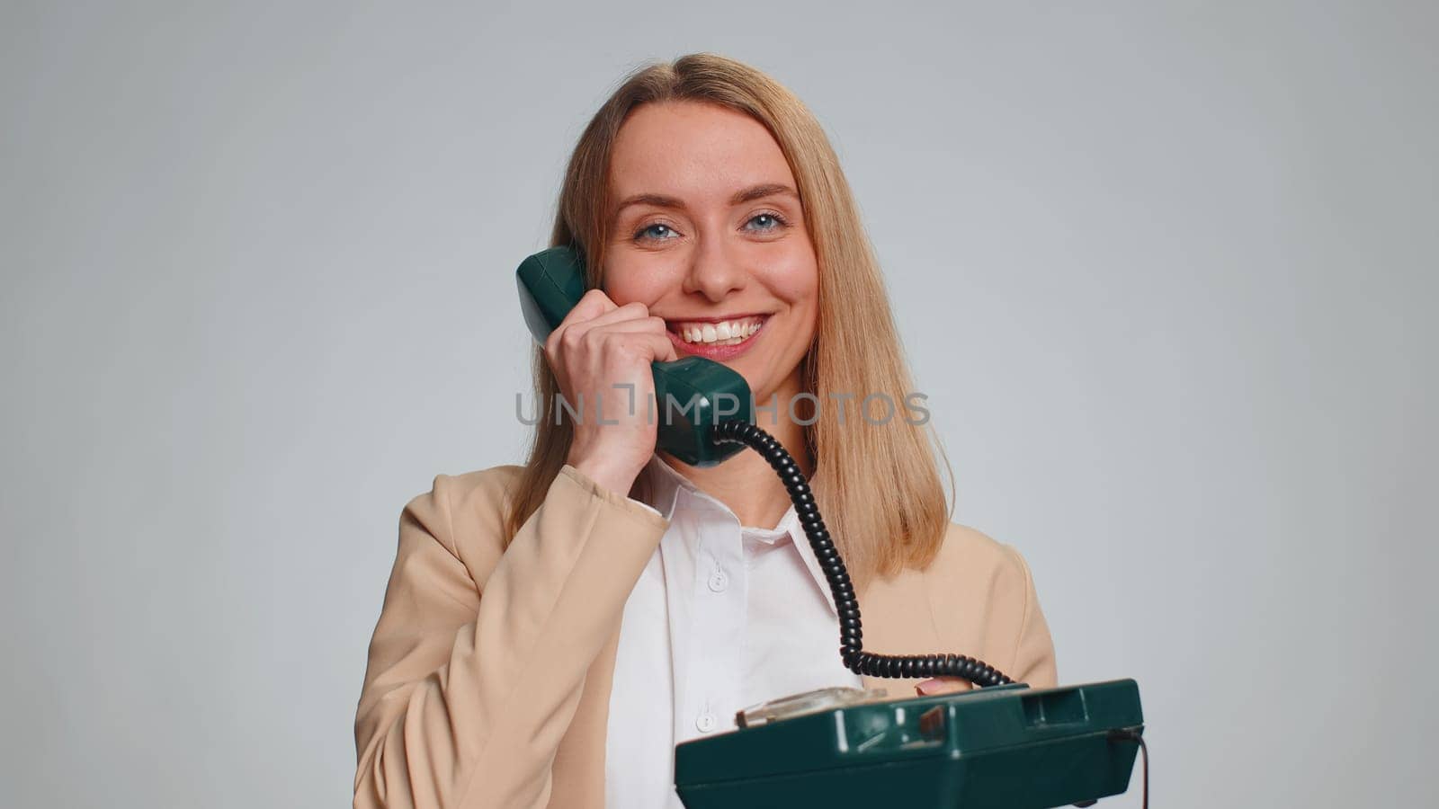 Hey you, call me back. Business woman talking on wired vintage telephone of 80s, says hey you call me back. Support service operator helpline. Girl in formal suit isolated on gray studio background