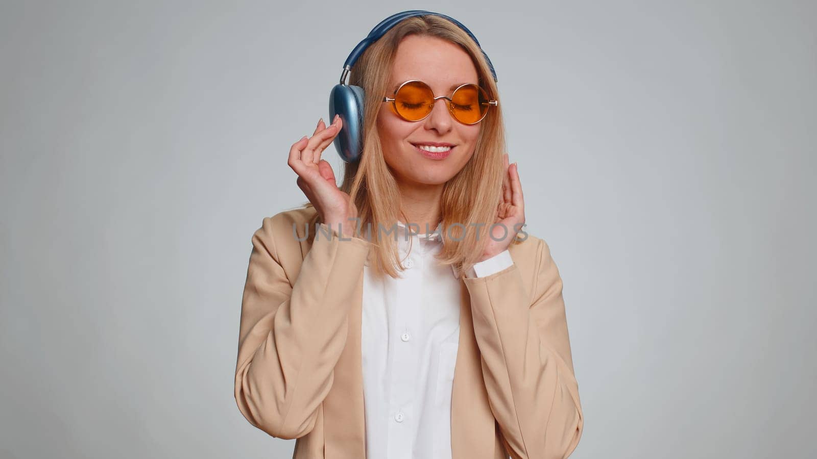 Happy business woman in headphones listening music and dancing disco fooling around having fun expressive gesticulating hands, relaxing on party. Girl isolated alone on studio gray wall background