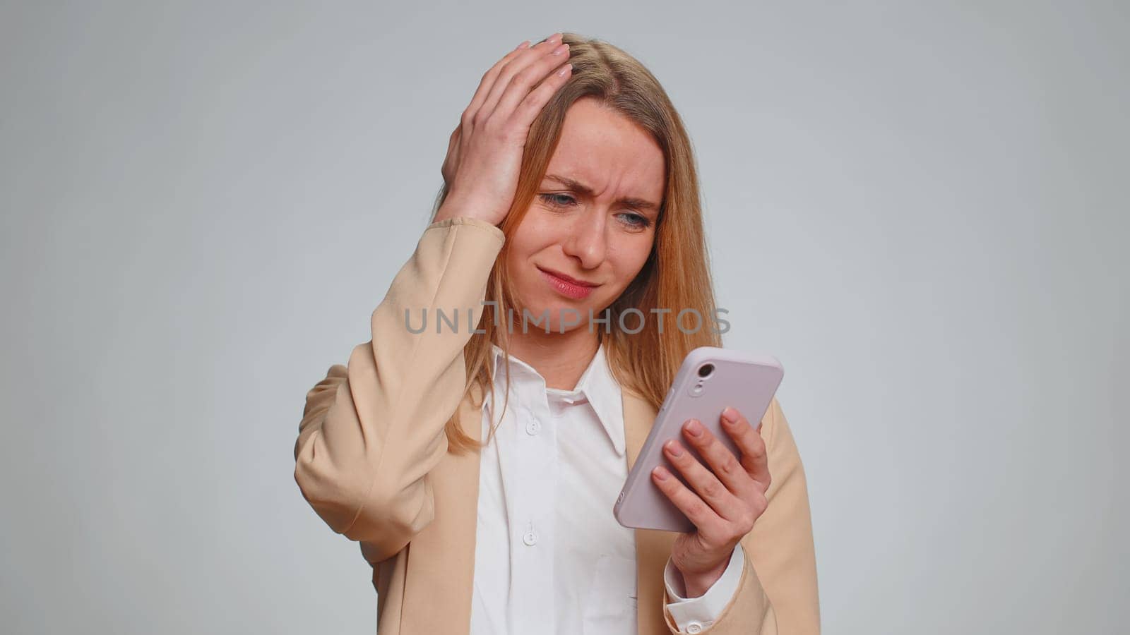 Sad business woman use mobile cell phone typing browsing, loses becoming surprised sudden lottery results, bad fortune, loss, fail. Unhappy girl isolated alone on gray studio wall background, indoors