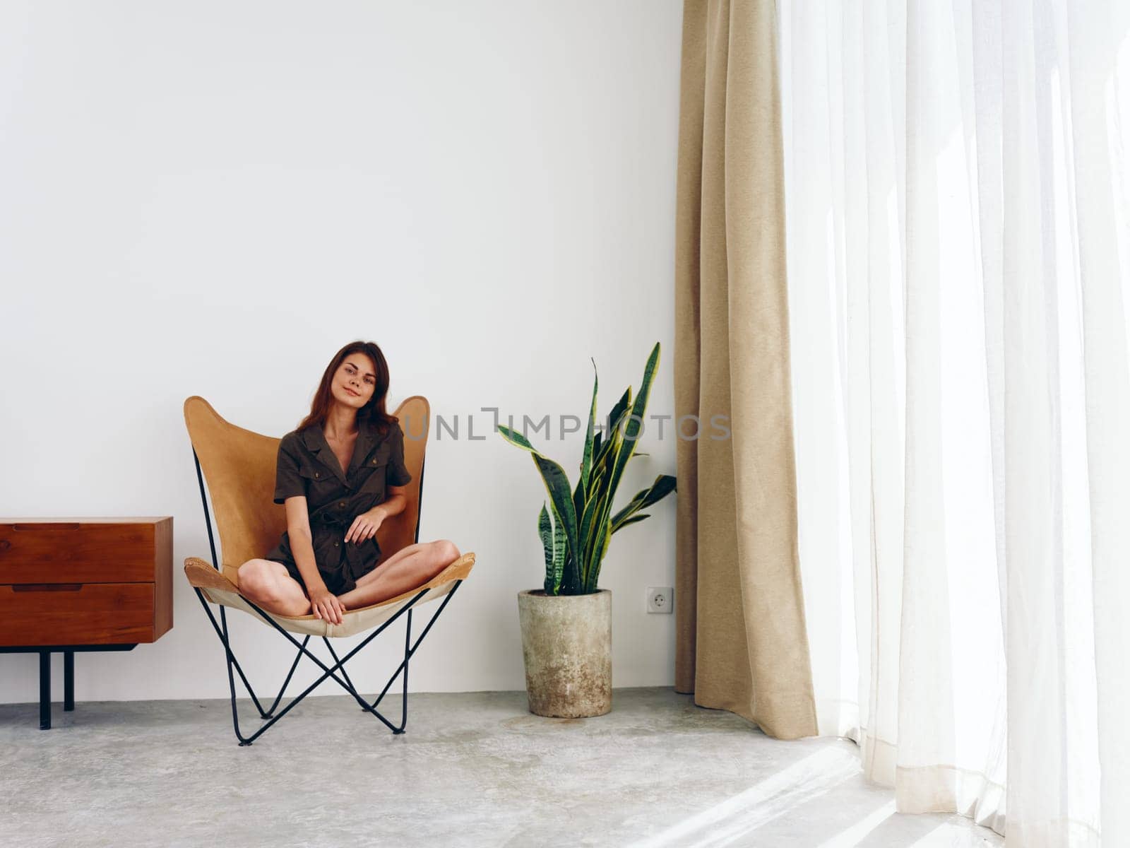 Woman sitting in a leather armchair near the window smiling , modern stylish interior Scandinavian lifestyle, copy space. High quality photo