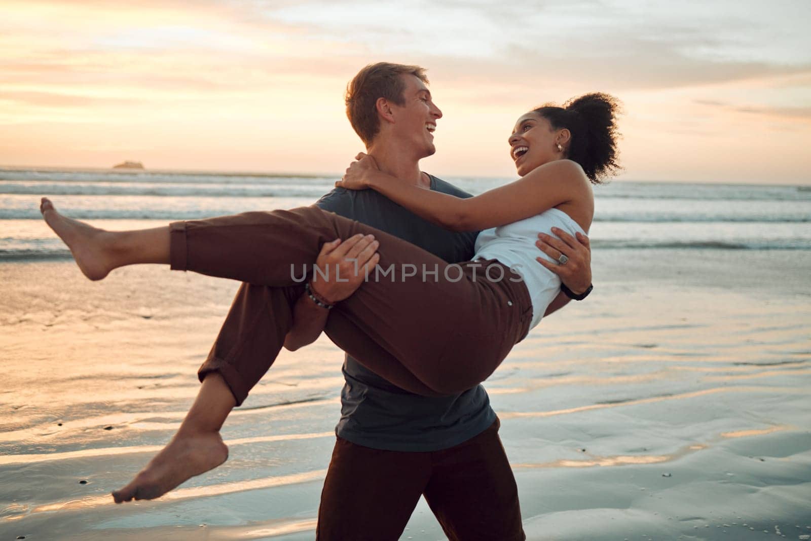 Man at beach lift woman with love, smile with sunset on travel holiday in Hawaii. Young couple travel to ocean on vacation, happy and play together with sunset at sea or waves in nature during summer.