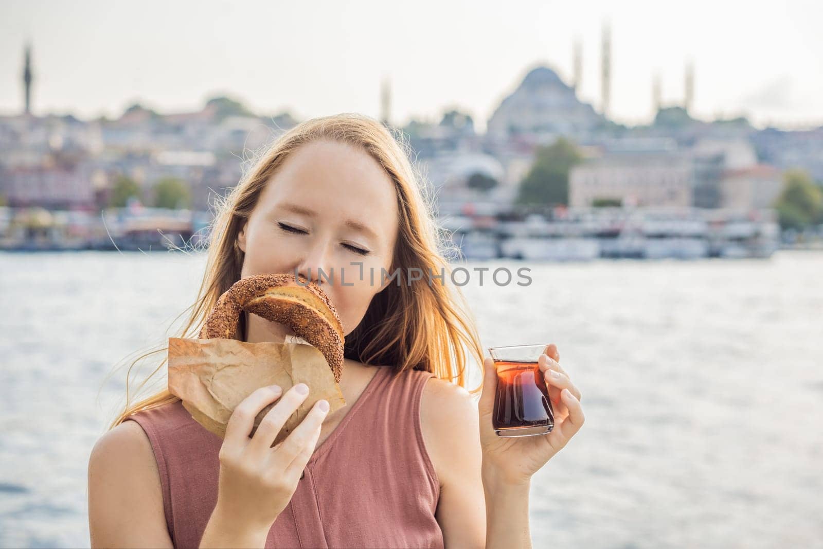 Woman in Istanbul having breakfast with Simit and a glass of Turkish tea. Glass of Turkish tea and bagel Simit against golden horn bay in Istanbul, Turkey. Turkiye.
