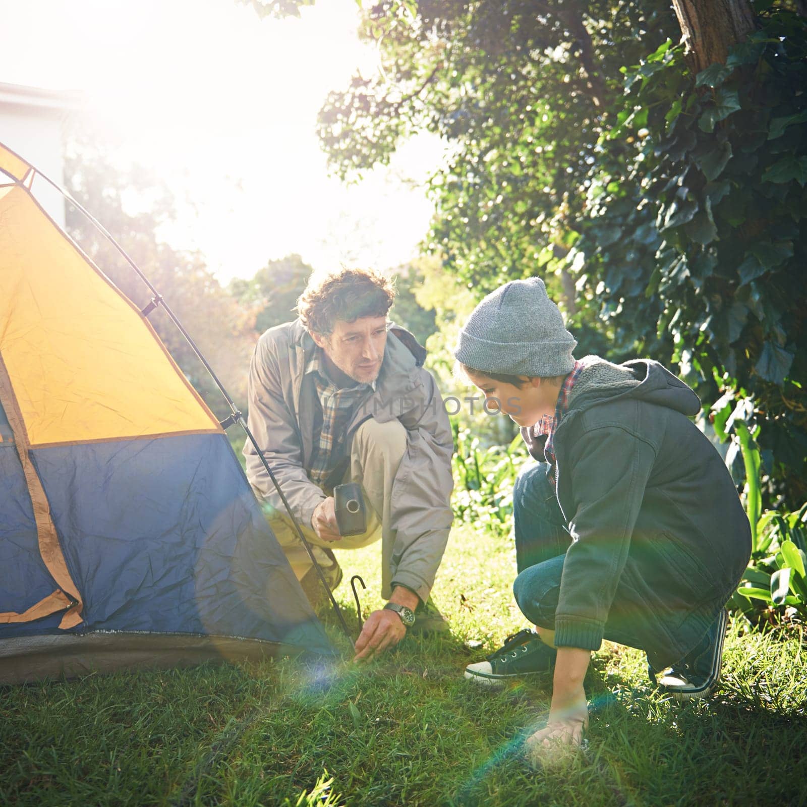 Father, child and hammer tent for camping outdoor in nature on vacation, bonding together and sunset. Dad, boy and preparing camp, learning and helping in forest for travel, holiday and adventure