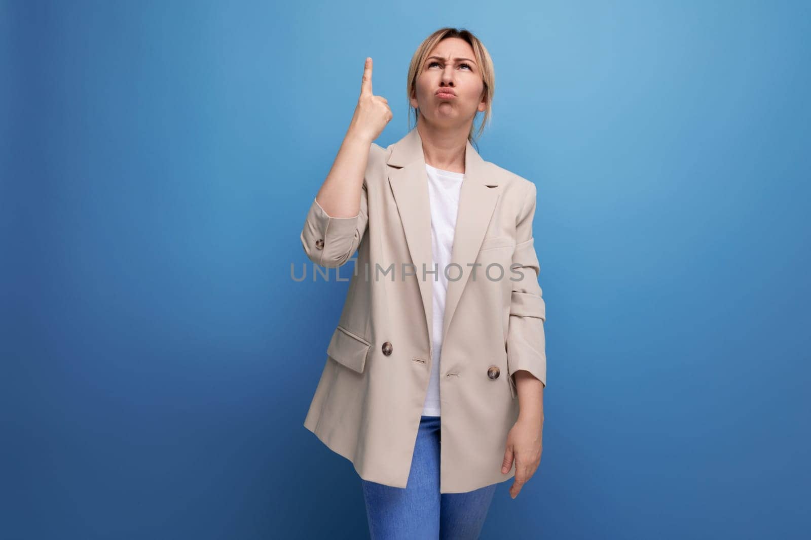 portrait of pensive european blonde 30s business woman with thumbs up on studio background.