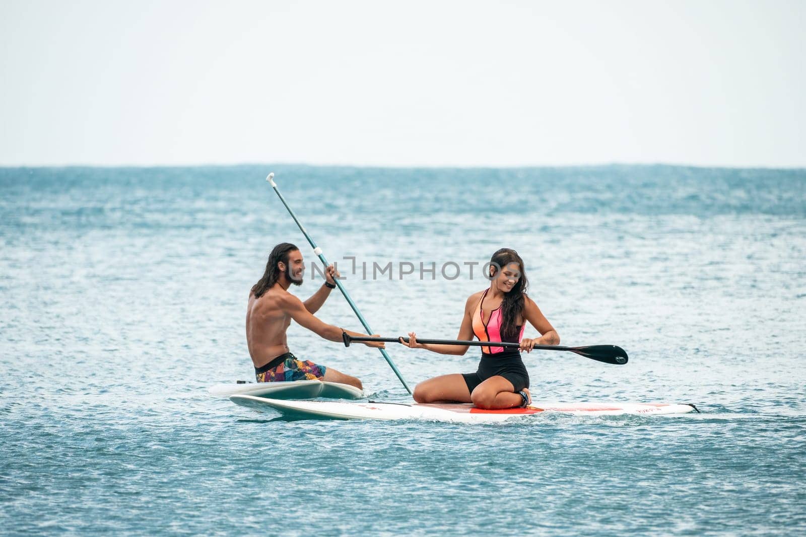 Sea woman and man on sup. Silhouette of happy young woman and man, surfing on SUP board, confident paddling through water surface. Idyllic sunset. Active lifestyle at sea or river