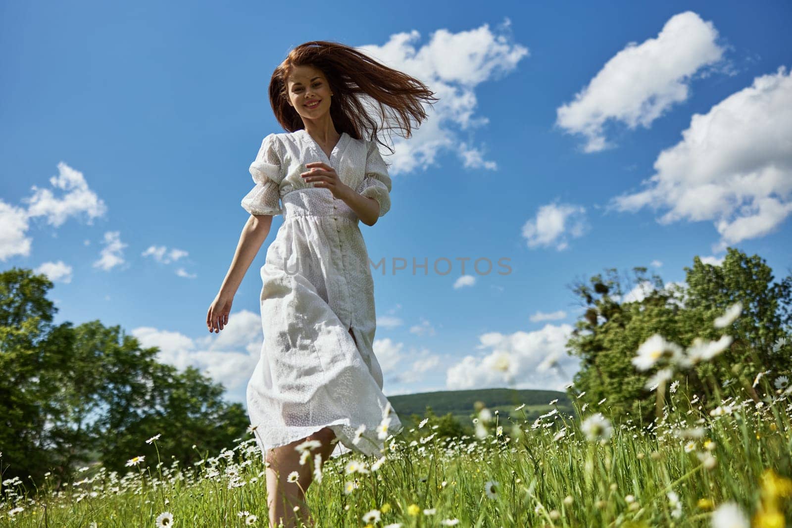 a happy woman in a light dress runs through a chamomile field against a clear sky. High quality photo