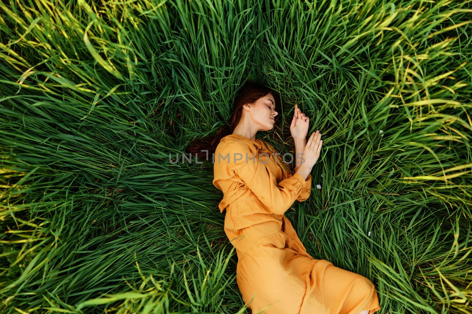 a relaxed woman enjoys summer lying in the tall green grass with her eyes closed. Photo taken from above by Vichizh