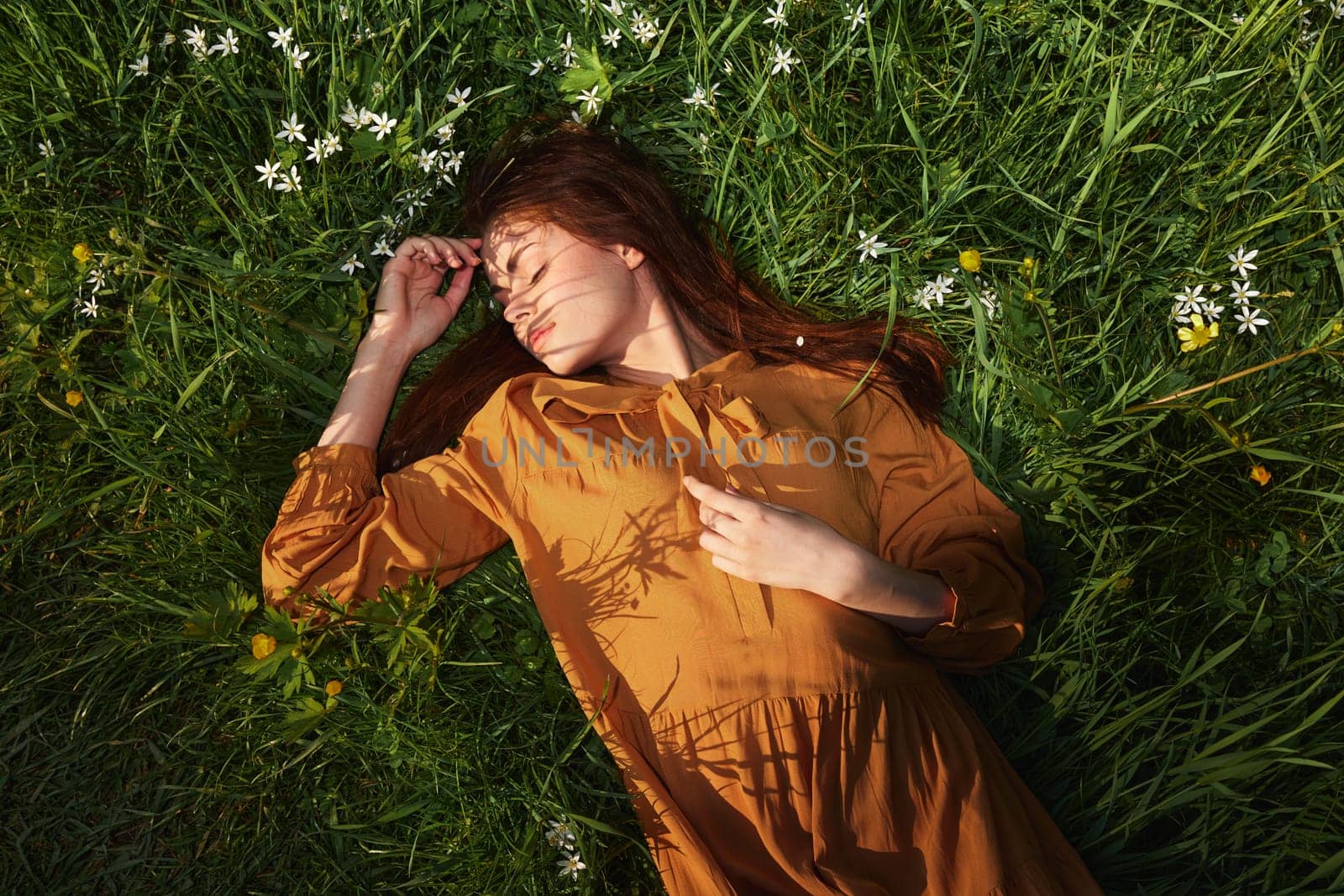a relaxed woman, resting lying in the green grass, in a long orange dress, with her eyes closed and a pleasant smile on her face, recuperating by Vichizh