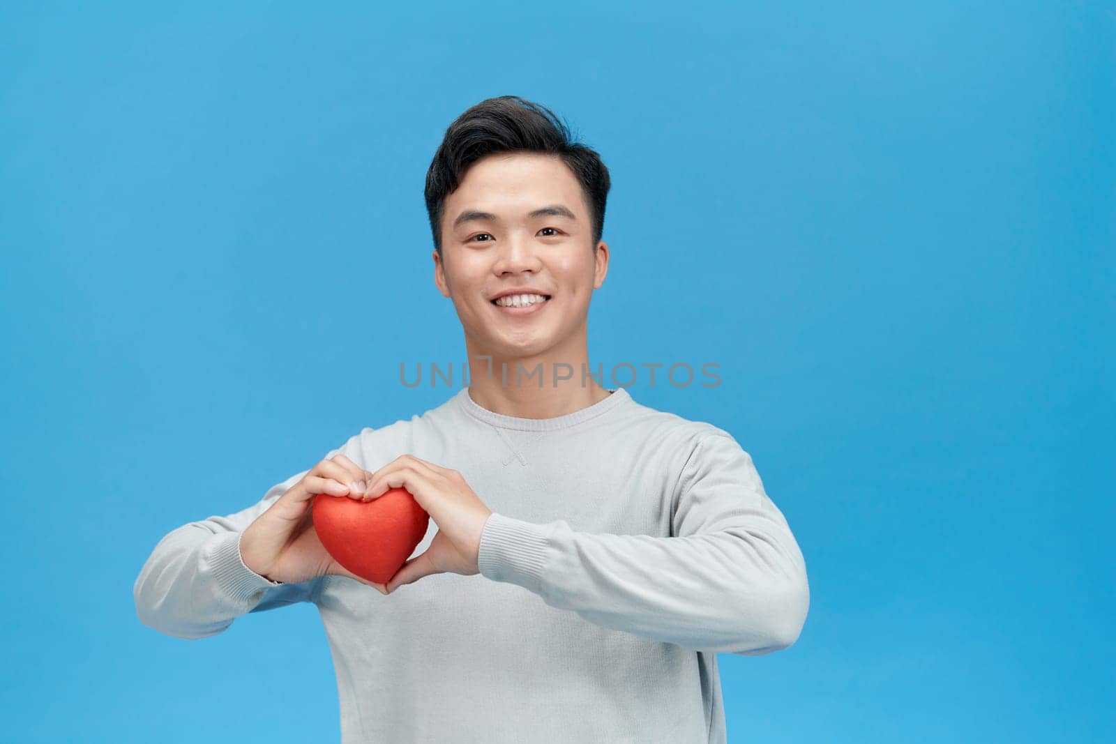 Young happy Asian man holding red heart ready for Valentine's day by makidotvn