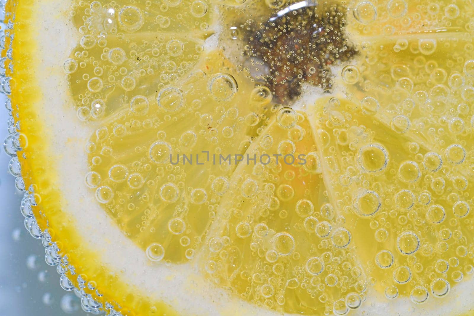 Close-up of a lemon slice in liquid with bubbles. Slice of ripe lemon in water. Close-up of fresh citron slice covered by bubbles. Macro horizontal image