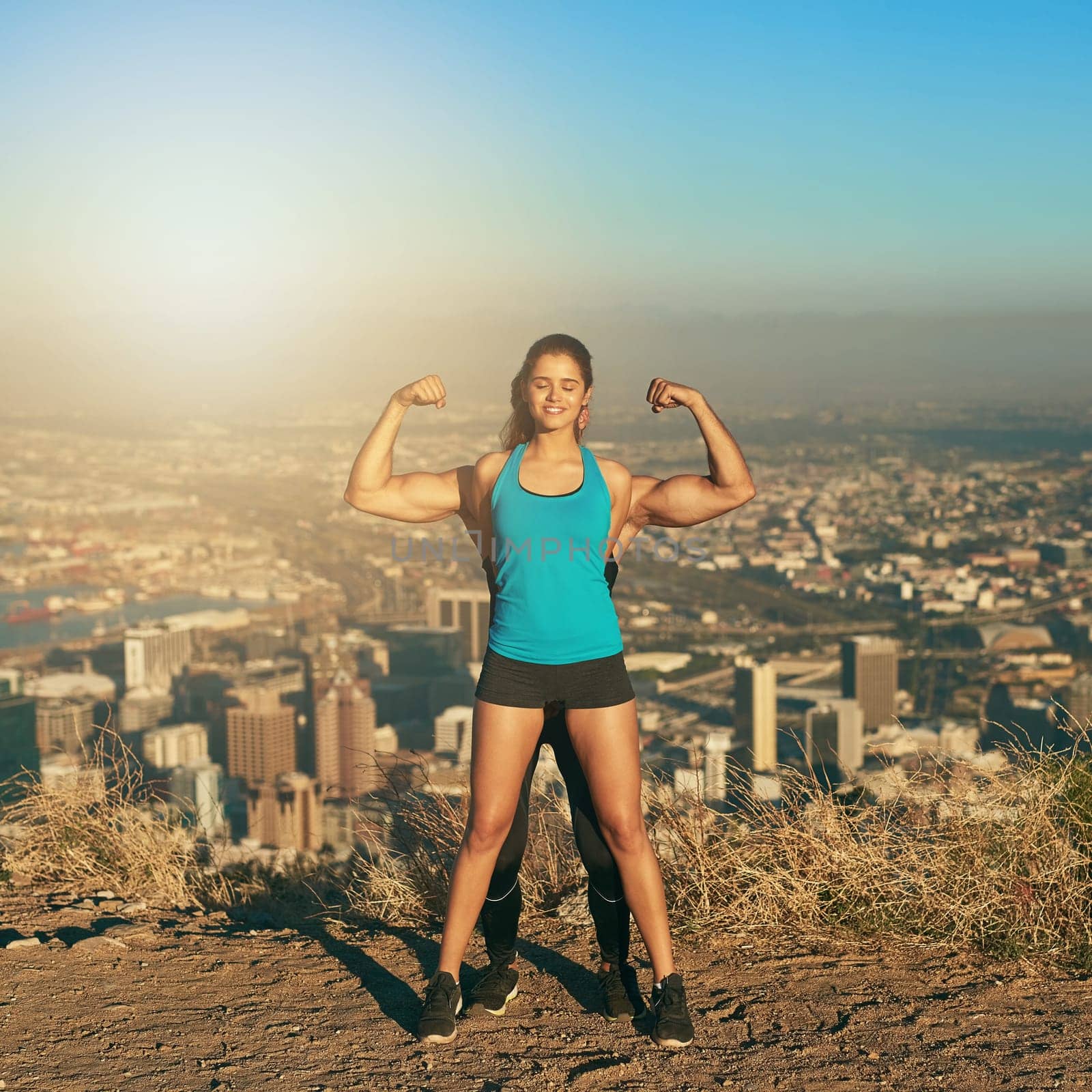 Showing off her guns. a young woman standing in front of her boyfriend whos flexing his muscles