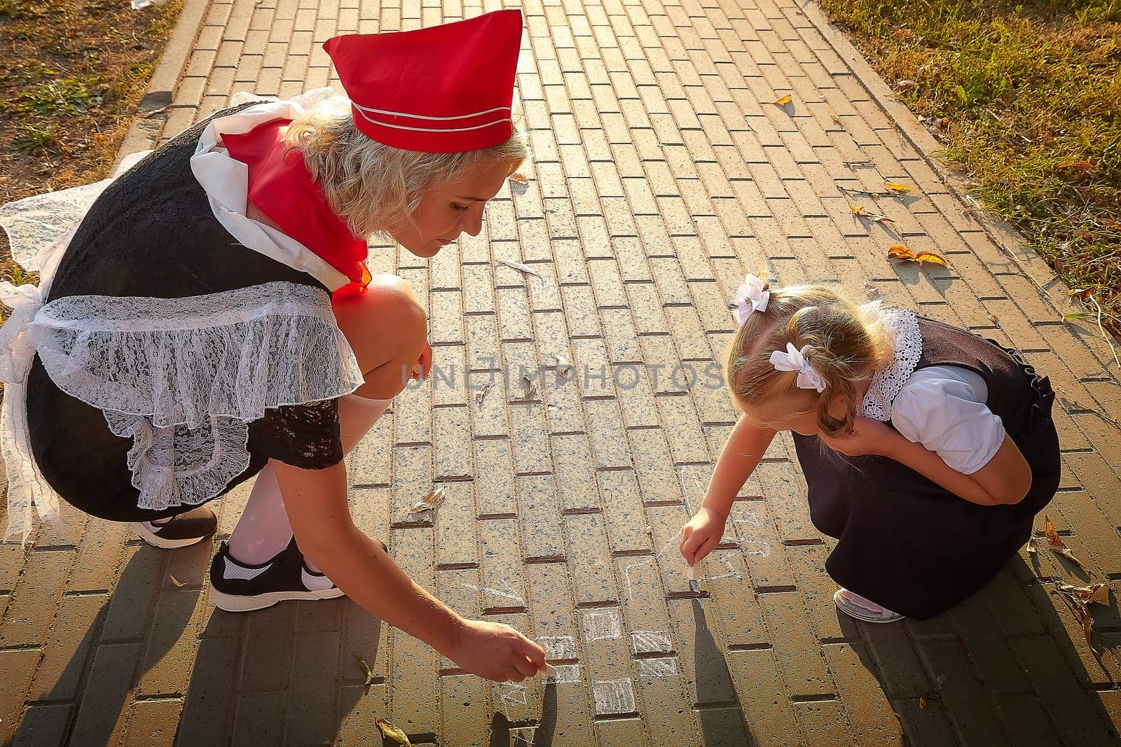 Young and adult schoolgirl on September 1 drawing by chalk on asphalt. Generation of schoolchildren of USSR and Russia. Female pioneer in red tie and October girl in modern uniform. Daughter and mom