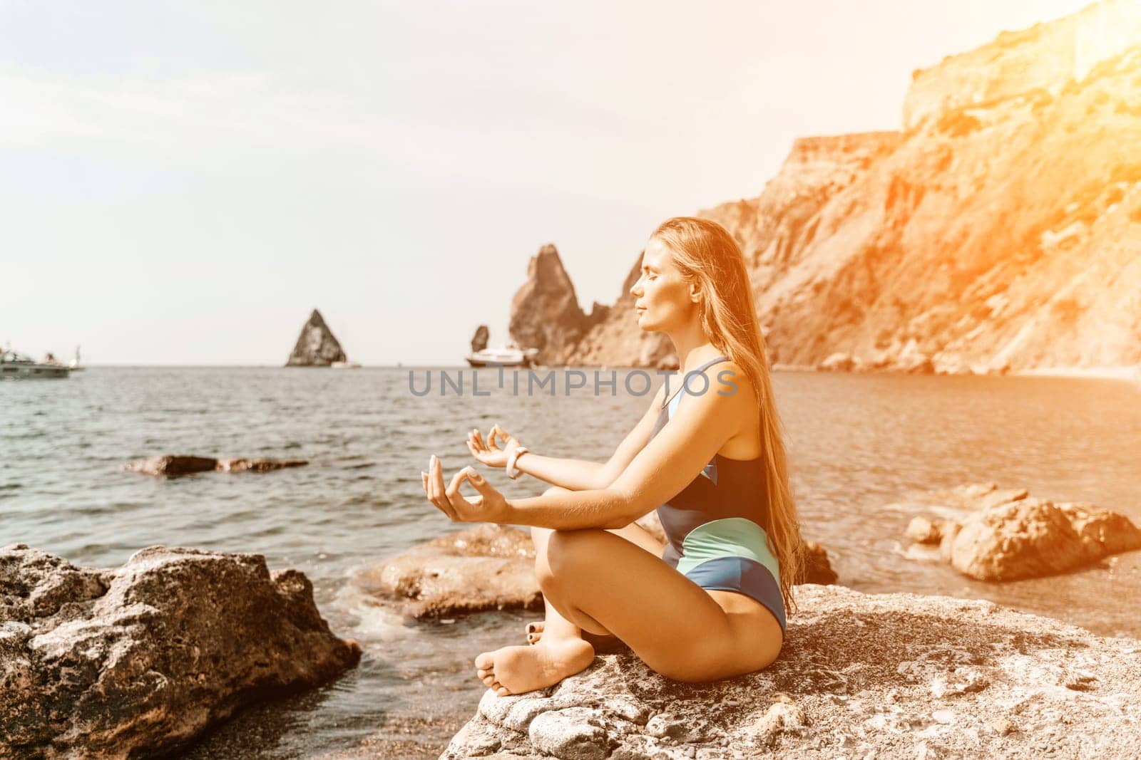 Yoga on the beach. A happy woman meditating in a yoga pose on the beach, surrounded by the ocean and rock mountains, promoting a healthy lifestyle outdoors in nature, and inspiring fitness concept. by Matiunina