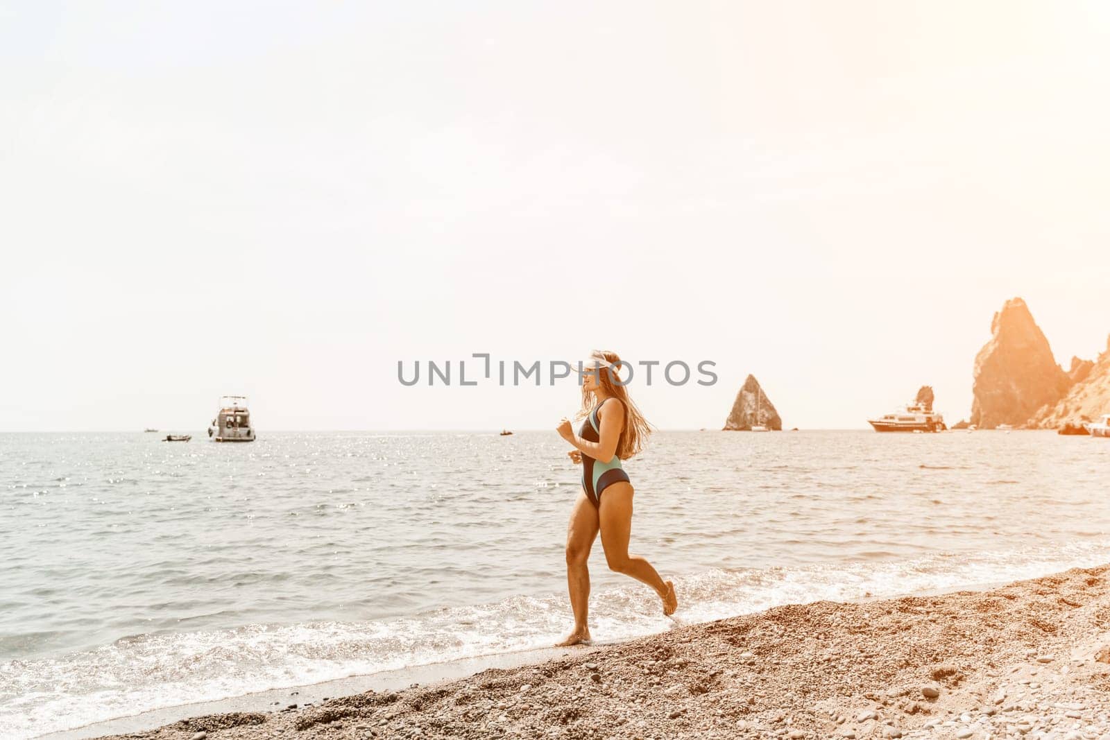 Woman travel summer sea. A happy tourist in a blue bikini enjoying the scenic view of the sea and volcanic mountains while taking pictures to capture the memories of her travel adventure