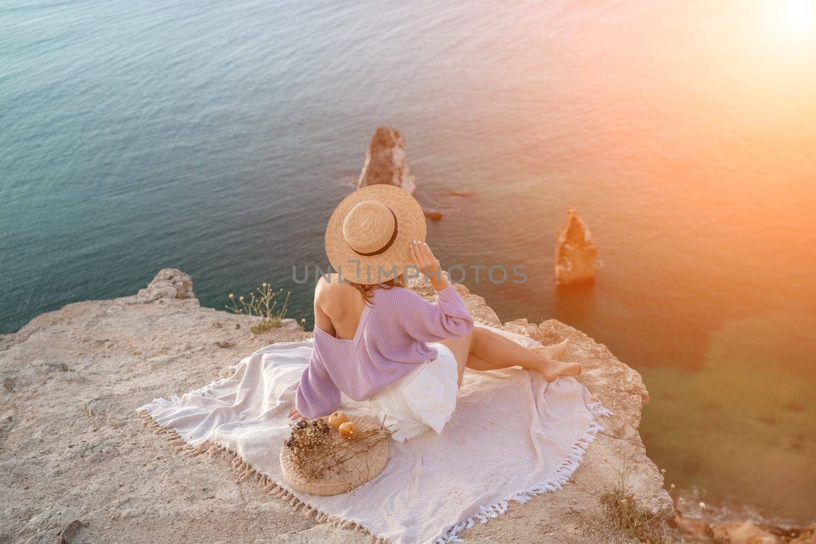 woman sea travel. photo of a beautiful woman with long blond hair in a pink shirt and denim shorts and a hat having a picnic on a hill overlooking the sea.