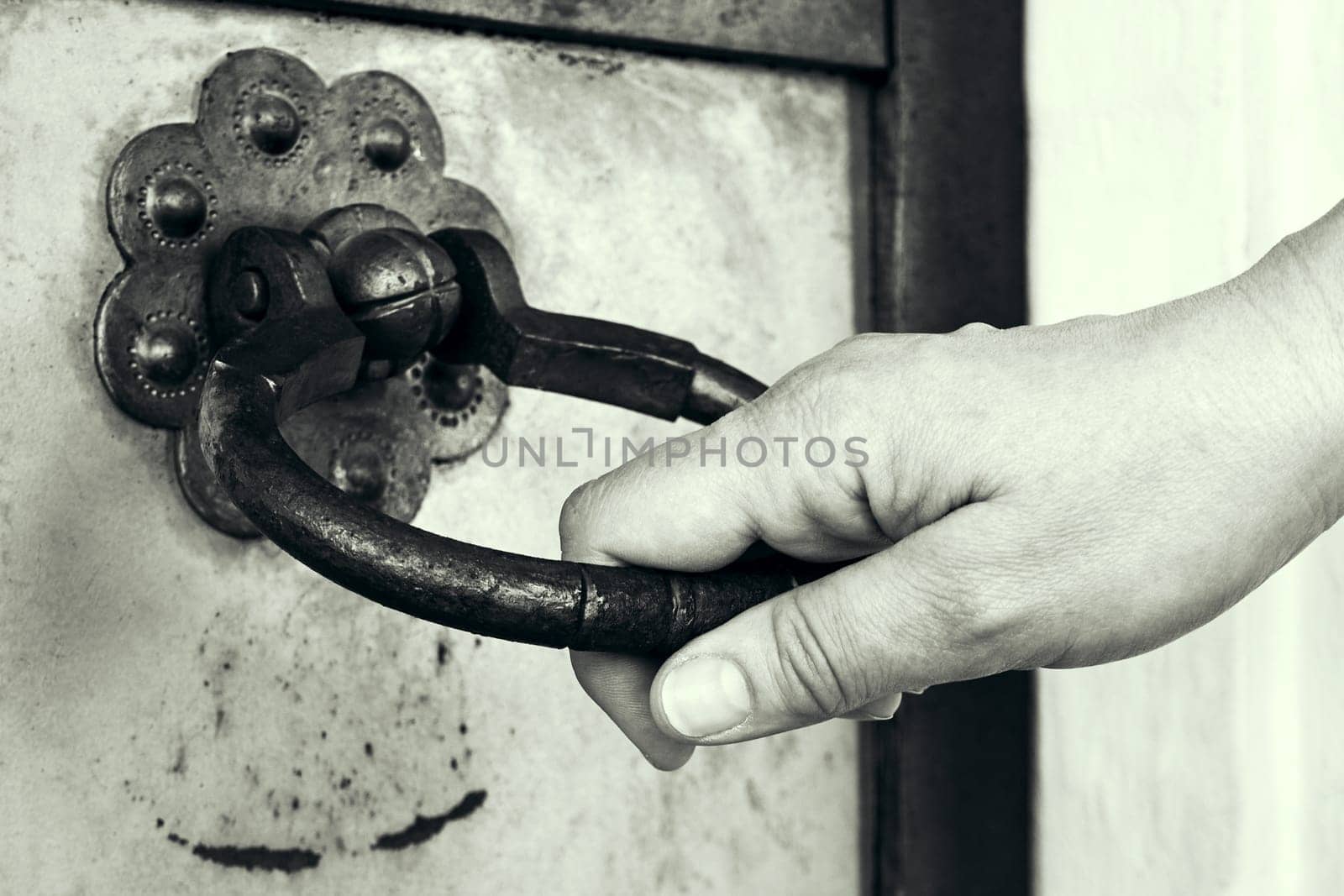 A hand opens an ancient door. Door handle in the form of a ring. Black and white toned image