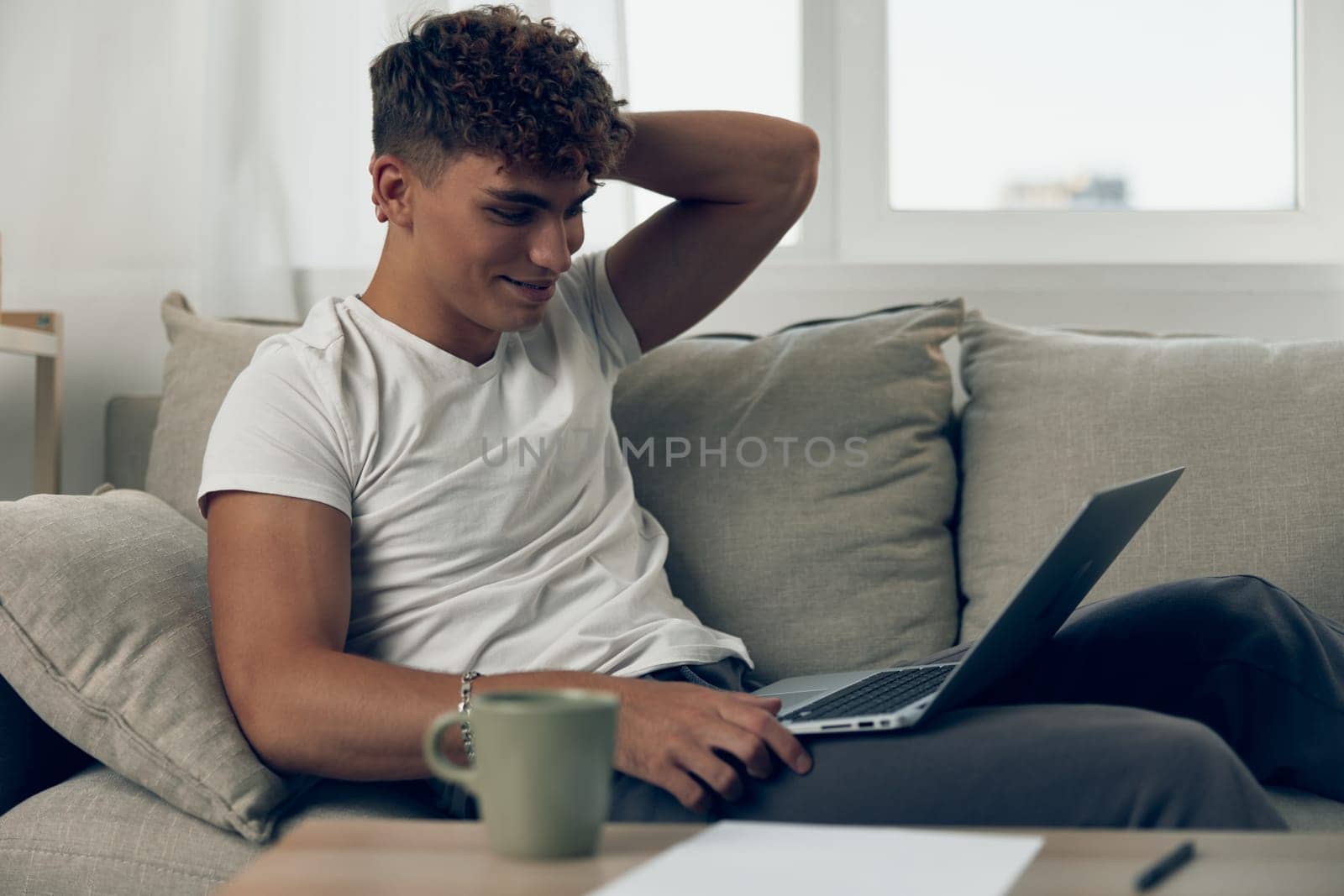 man sofa freelance laptop adult caucasian typing white phone modern browsing person curly by SHOTPRIME