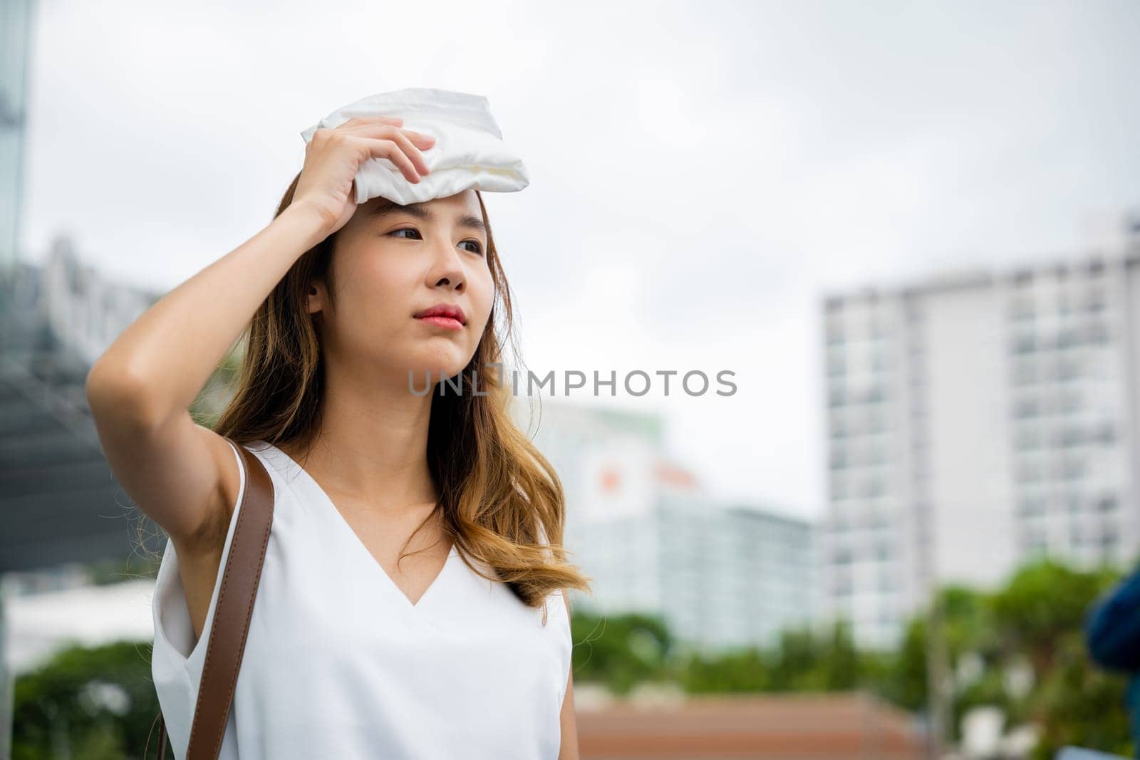 Asian beautiful business woman drying sweat her face with cloth in warm summer day hot weather, Female having sunstroke skin damage from sun UV city air pollution outdoors on street