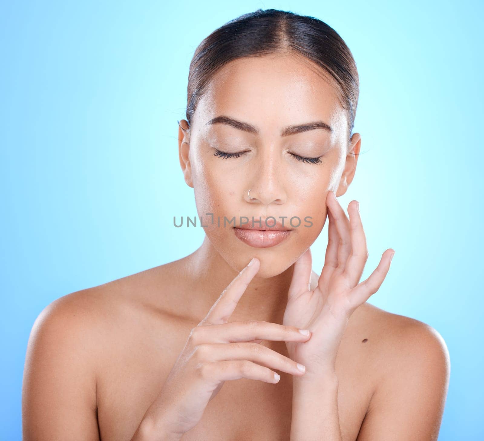 Skincare, woman and hands on face in studio for makeup, wellness or gentle cleaning on blue isolated background. Person, beauty and girl skin model relax in luxury, facial and cosmetic treatment by YuriArcurs