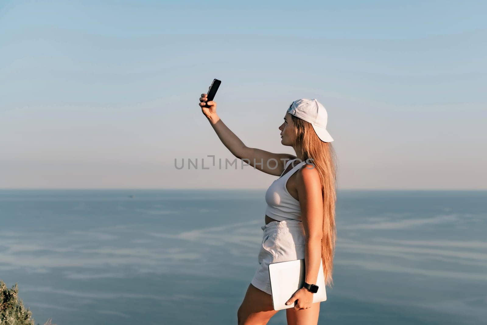 Selfie woman in a cap, white tank top and shorts makes a selfie shot mobile phone post photo social network outdoors on the background of the sea beach people vacation lifestyle travel concept