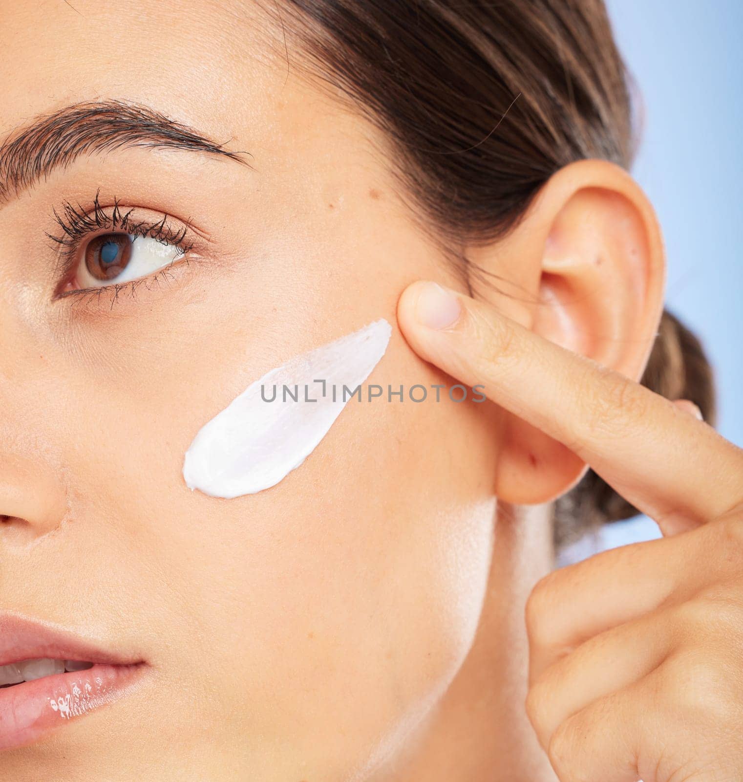 Face, beauty skincare and woman with cream in studio isolated on a blue background. Thinking, cosmetics and female model apply facial lotion, creme and moisturizer product for healthy skin hydration