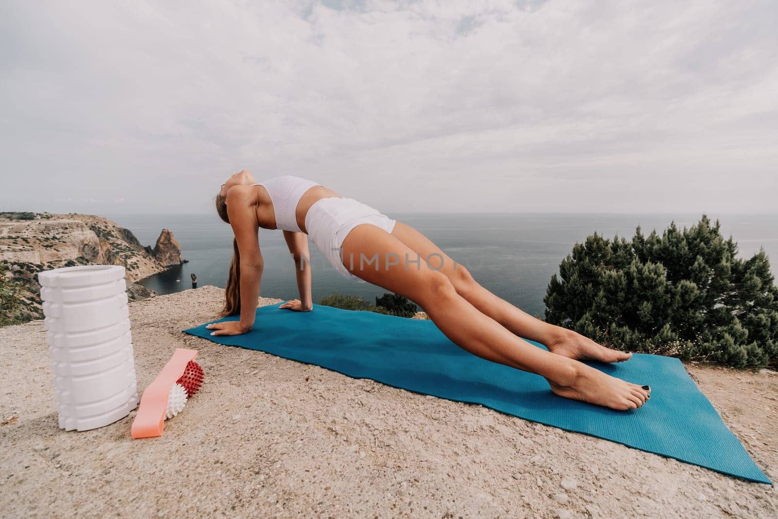 Woman sea pilates. Sporty, middle-aged woman practicing pilates in park near the sea. trains on a yoga mat and exudes a happy and active demeanor, promoting the idea of a healthy lifestyle through exercise and meditation.