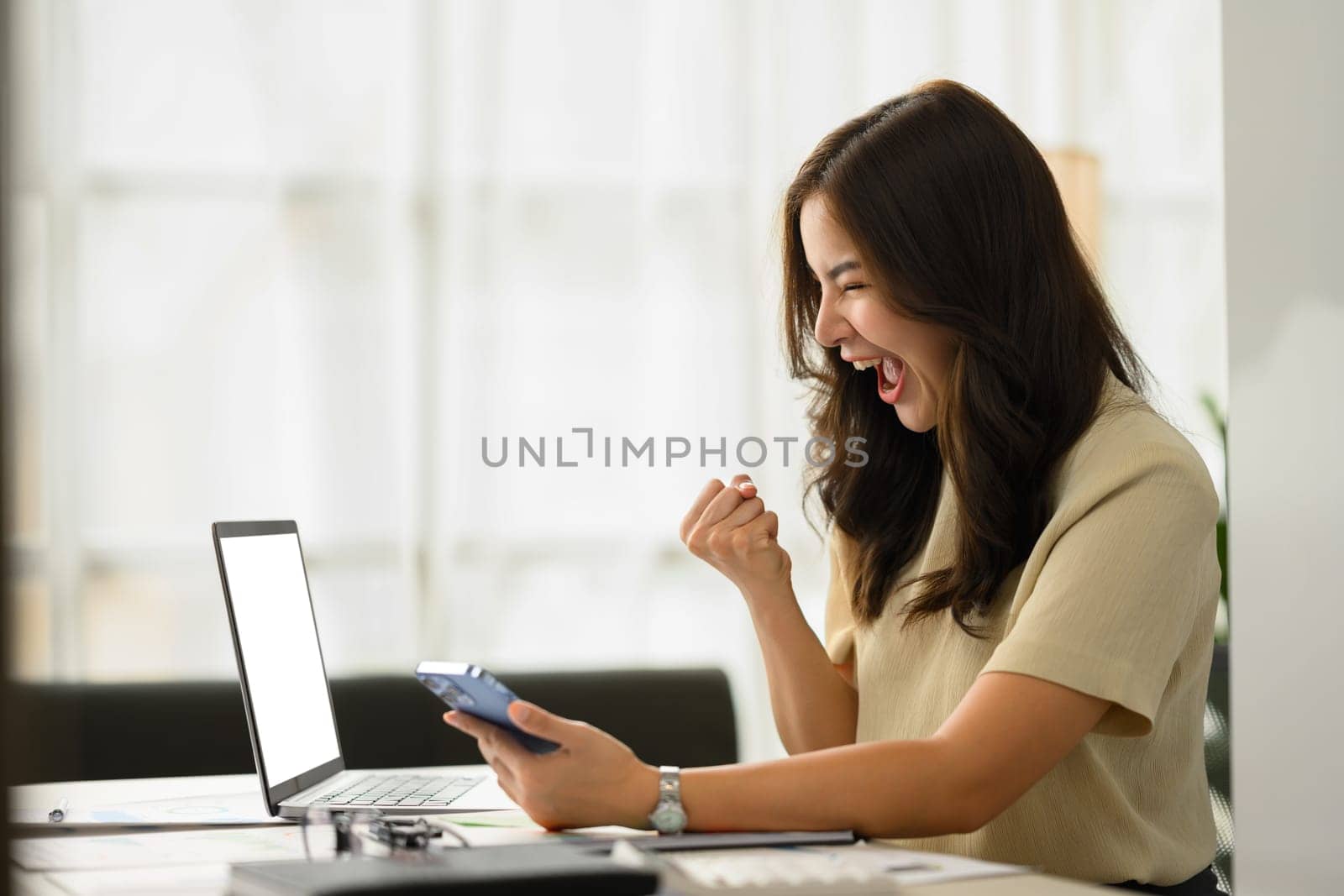 Side view of surprised young woman looking at smartphone, making winner yes gesture, reciting great massage.