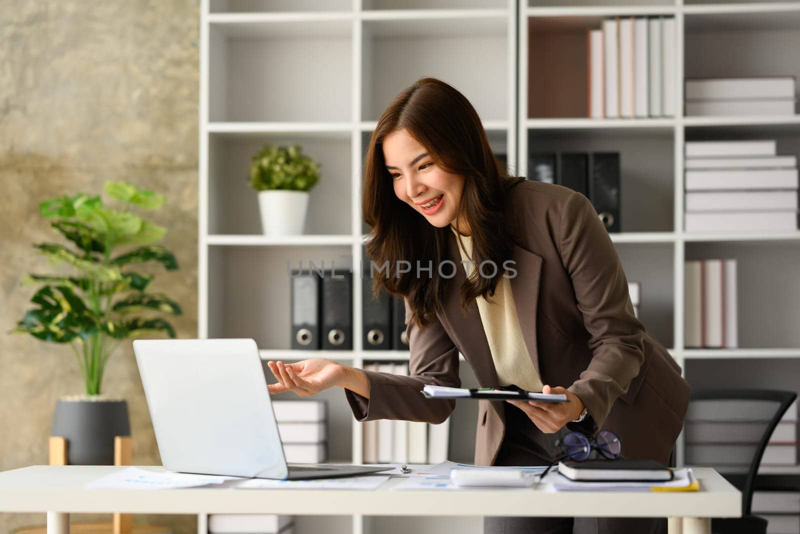 Cheerful female entrepreneur in trendy suit having video call in laptop at modern office.