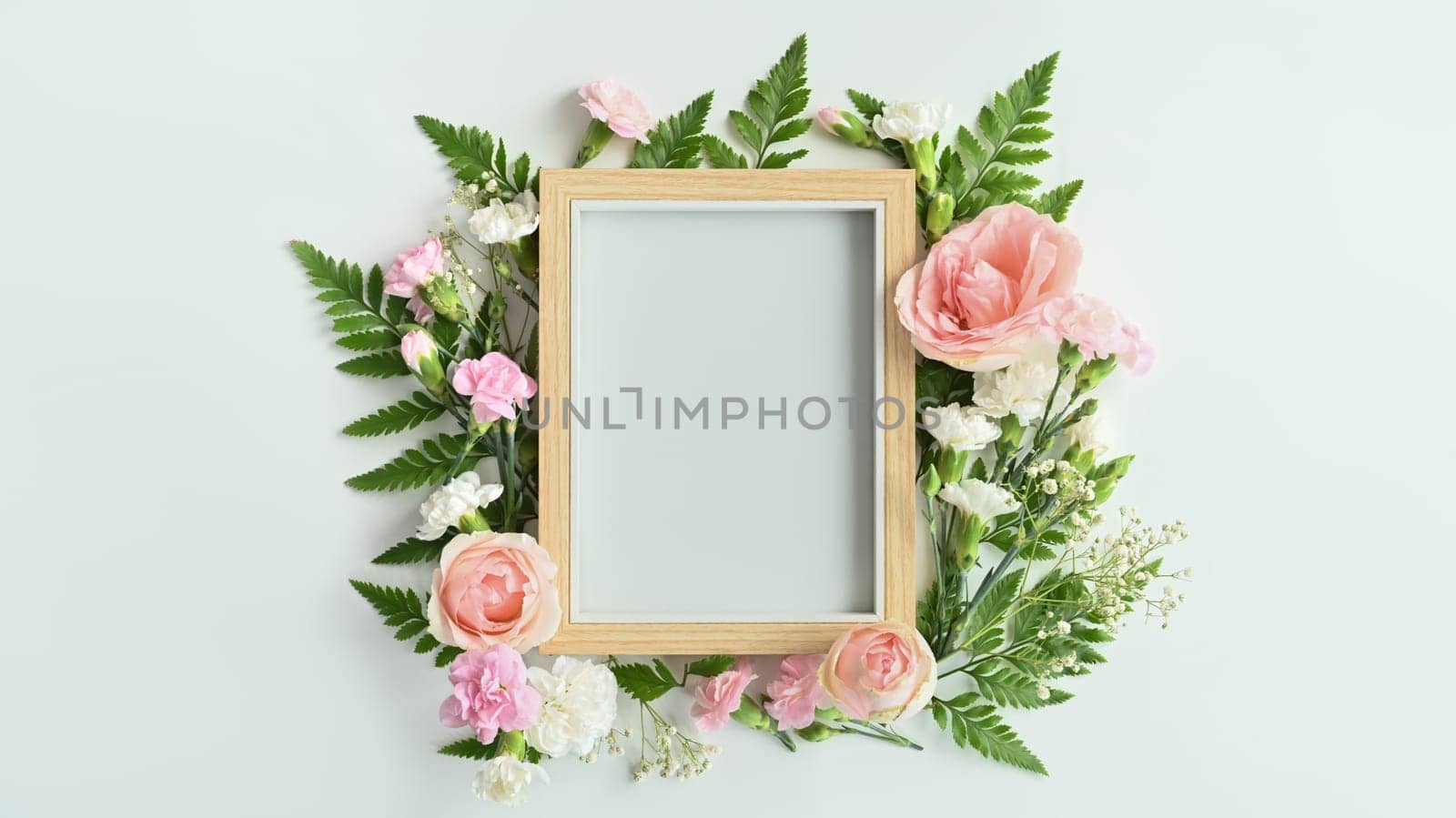 Wooden picture frame with pink rose, carnation and fern leaves on white background. Spring floral background, copy space by prathanchorruangsak