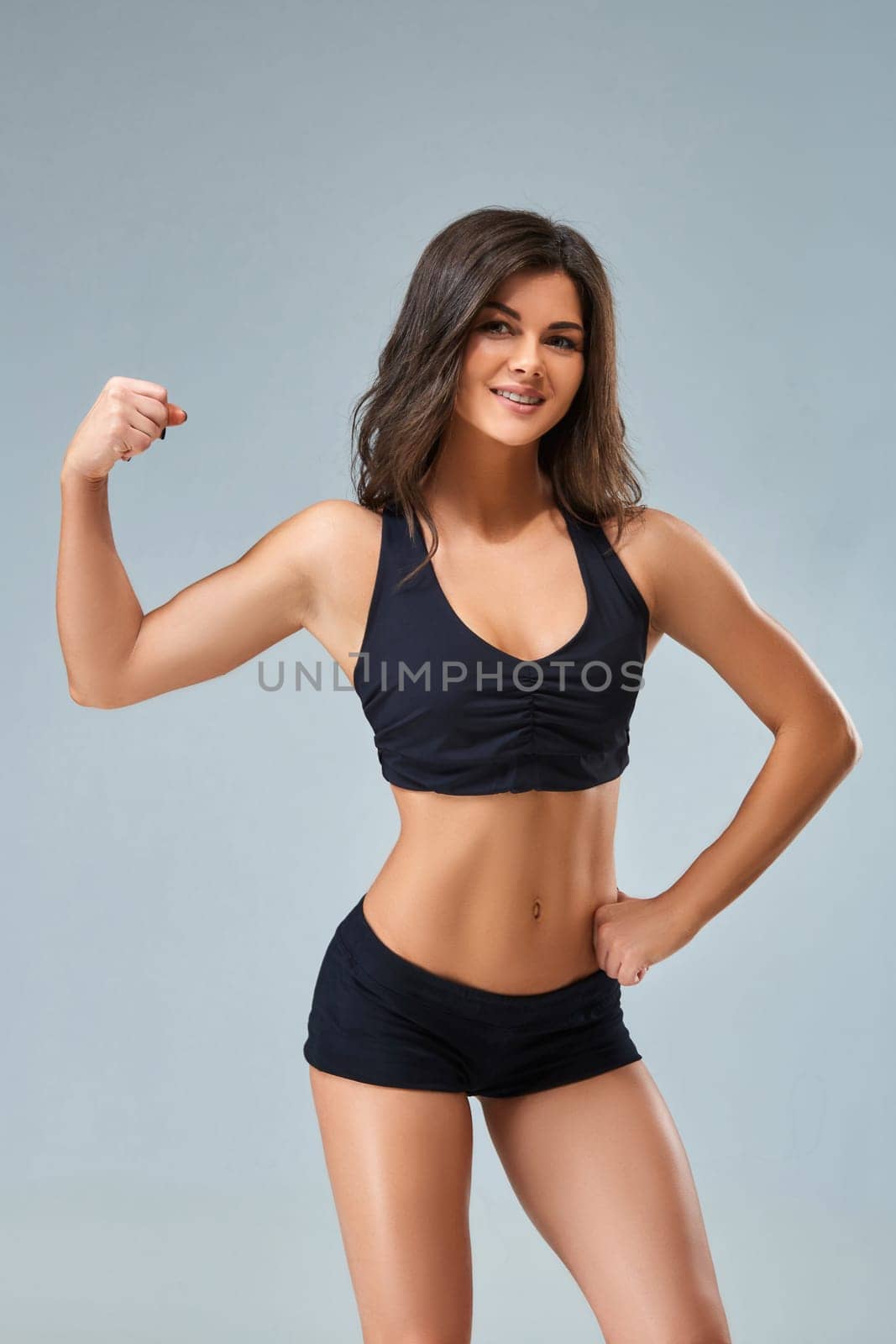 the sports and beautiful young girl on a gray background. The lovely girl with a sports figure and a beautiful smile. The beautiful girl in a topic poses and shows press.