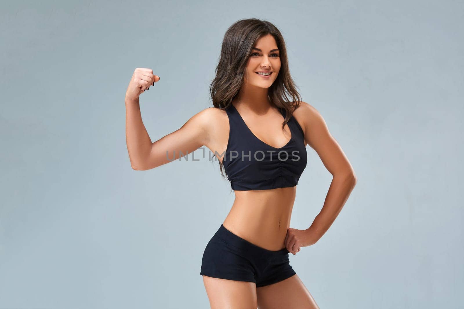 the sports and beautiful young girl on a gray background. The lovely girl with a sports figure and a beautiful smile. The beautiful girl in a topic poses and shows press.