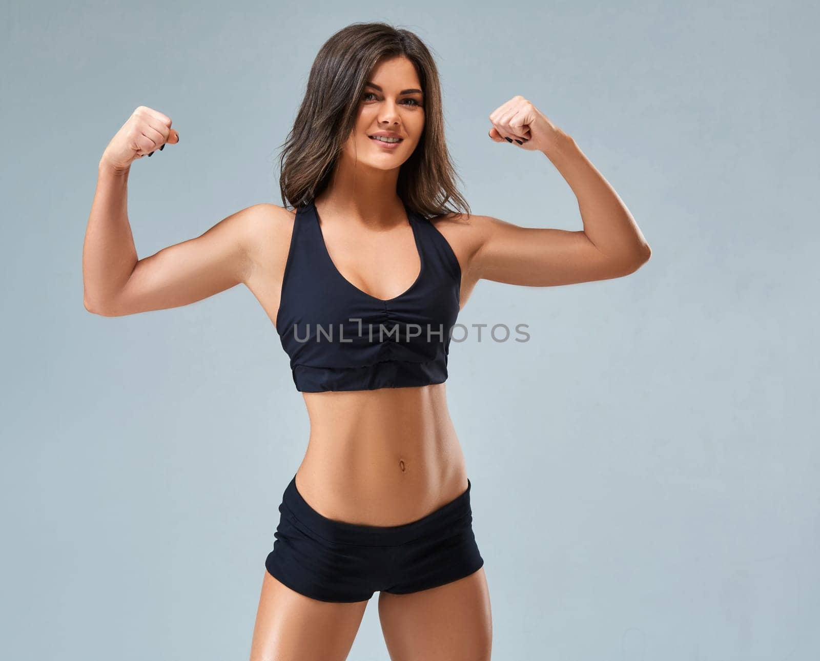 the sports and beautiful young girl on a gray background. The lovely girl with a sports figure and a beautiful smile. The beautiful girl in a topic poses and shows press.