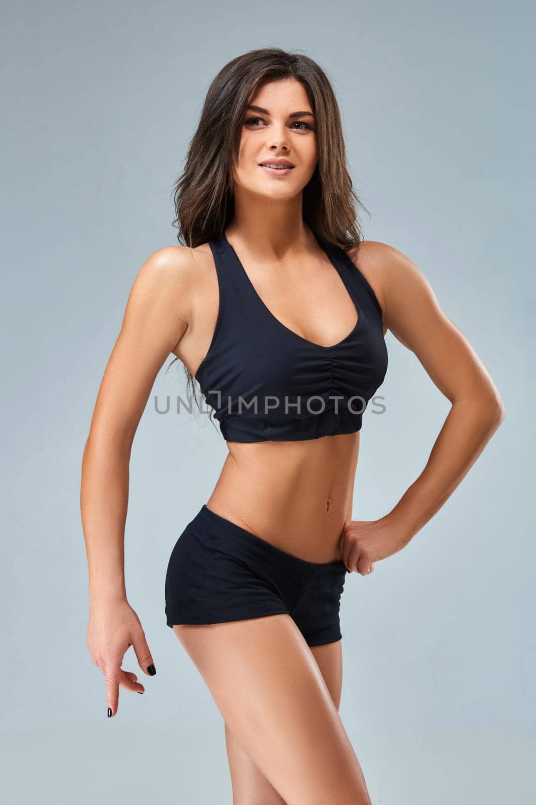 Young woman standing on grey background. Muscular female looking at camera. Female bodybuilder ready for gym exercise.