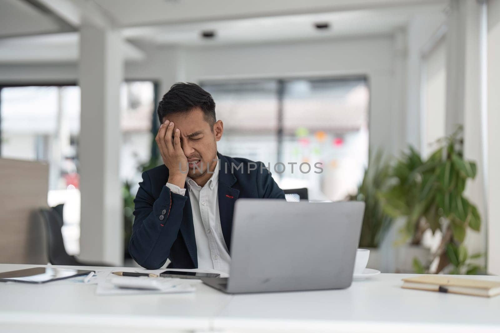 Tired exhausted business man office worker sitting at his desk tired of working in a laptop, overworked, having a headache, closed his eyes, needs rest and break.