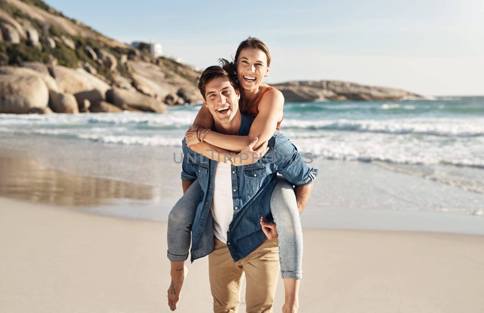 Couple, portrait and piggyback with smile at beach in summer sunshine for love, romance and bond for travel. Man, woman and happy with hug, ocean waves and trust in nature, outdoor and sea holiday.