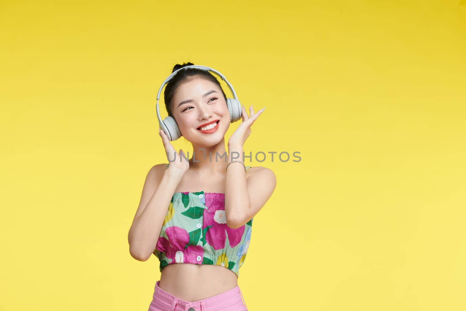 young woman singing while listening music with headphones isolated over yellow background