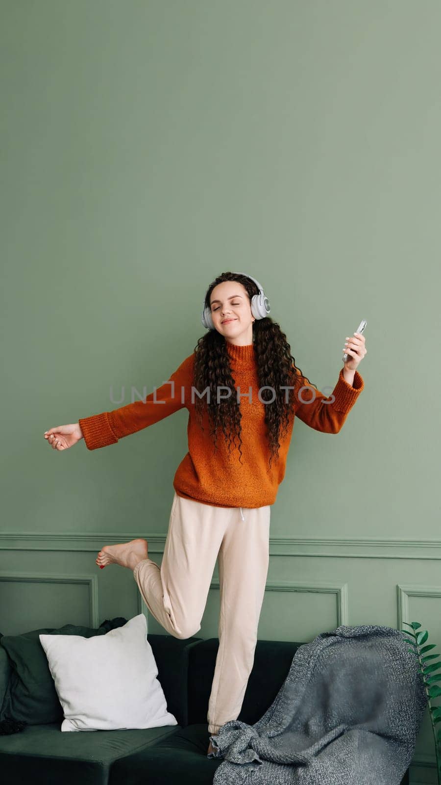 Joyful young woman dancing to her favorite music at home. Happy girl experiencing joy while listening to popular music with headphones. Pretty girl having fun and dancing to music in her living room.