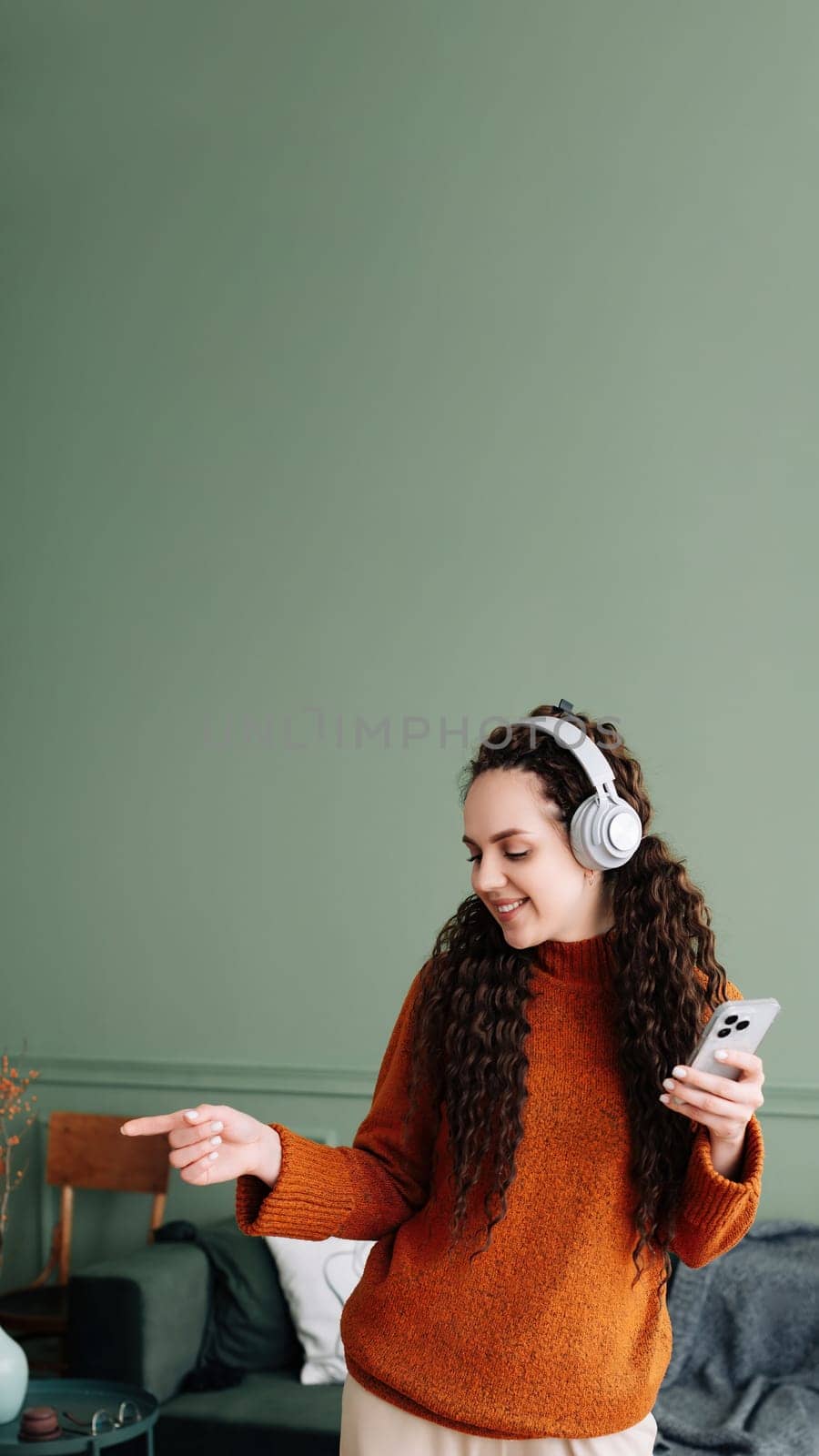 Enjoying the beats: woman dancing to music on phone with headphones in living room. Happy woman dancing while listening to music on smartphone with headphones