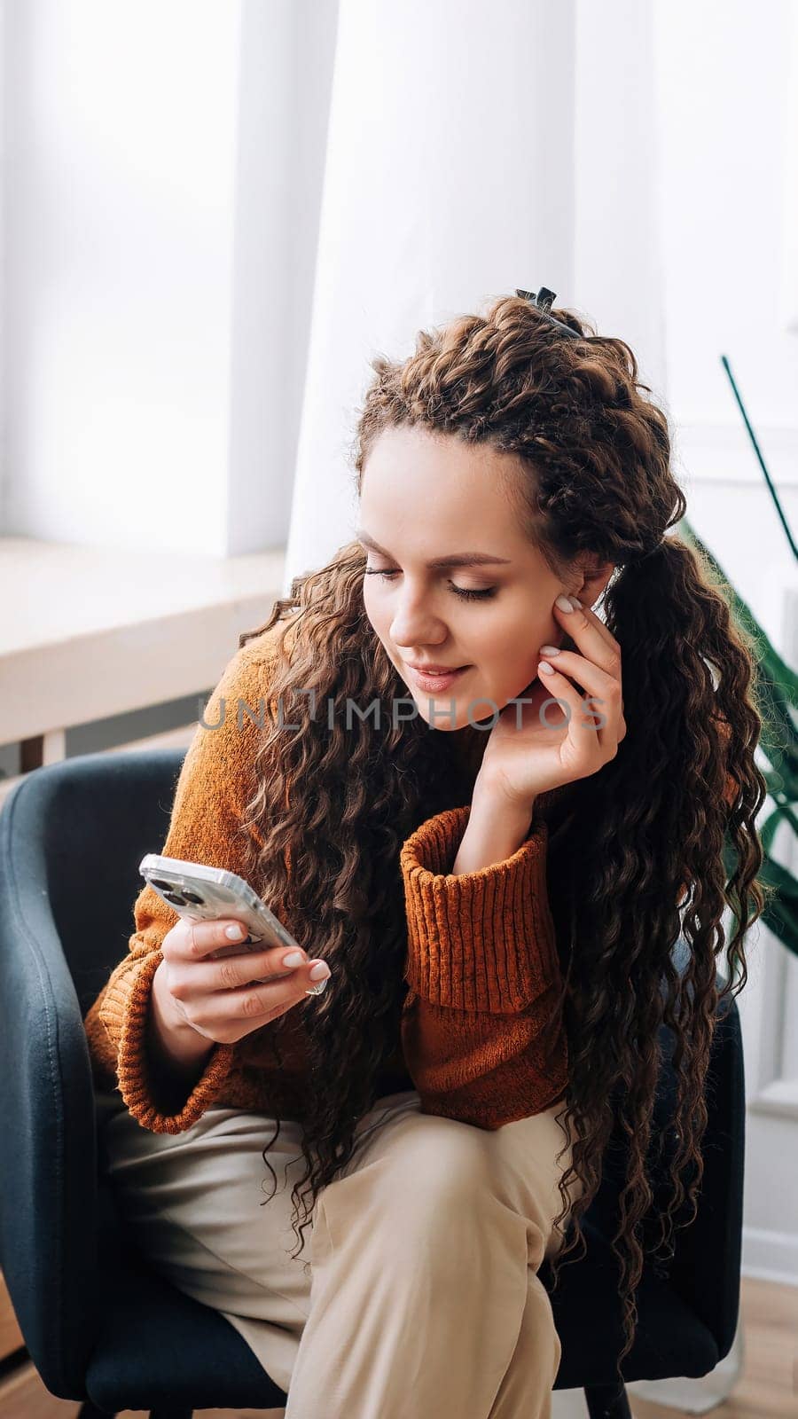 Relaxed woman browsing modern apps and texting messages on smartphone at home. Happy lady using mobile phone for internet browsing and online shopping. Mobile phone user messaging, shopping from home.