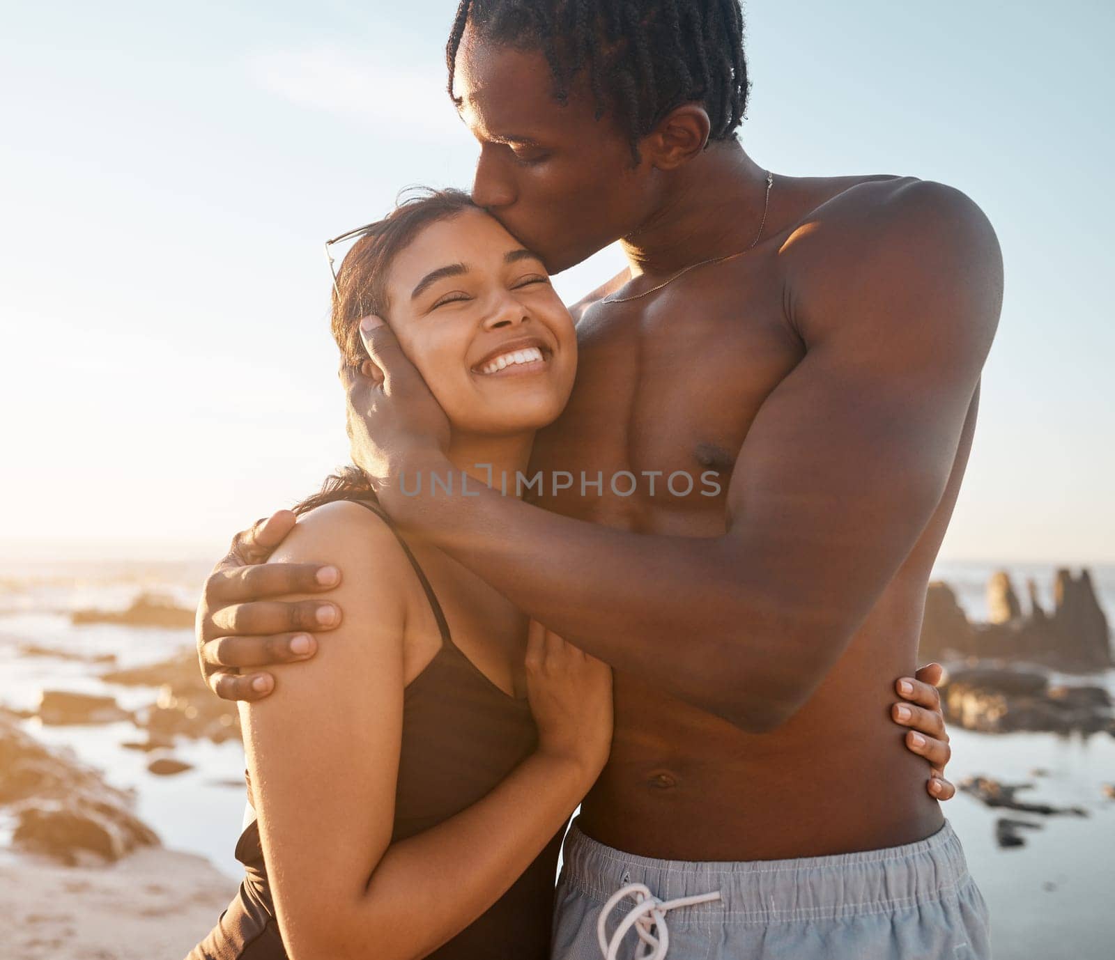 Couple hug or forehead kiss on sunset beach in relax romance holiday, love vacation date or bonding summer. Smile, black woman or kissing man in swimwear embrace, trust or travel support by ocean sea.