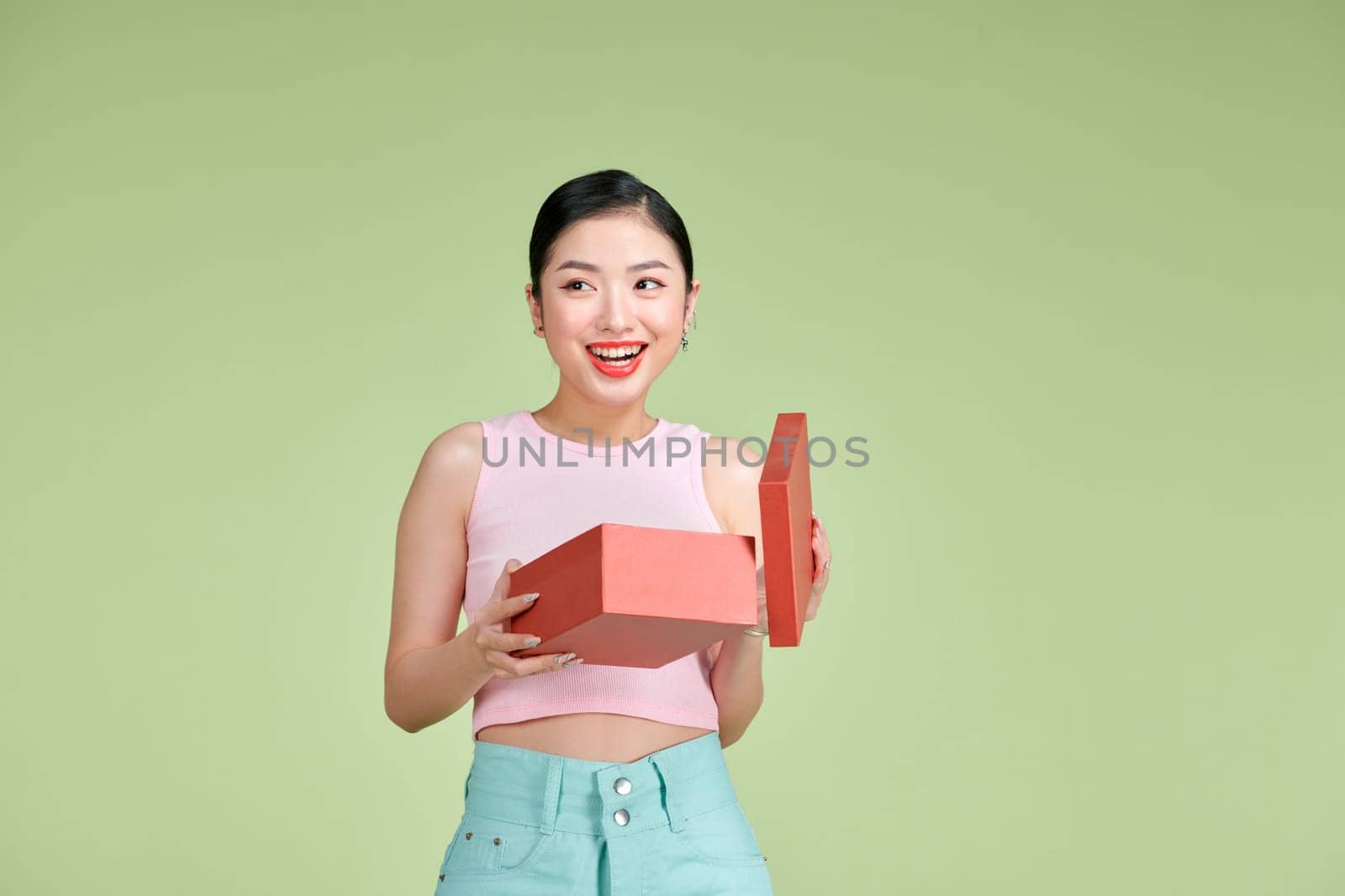 Happy young woman opening present for Valentine's Day on green studio background, 