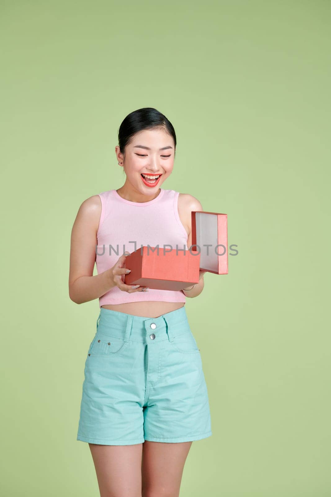 Happy young woman opening present for Valentine's Day on green studio background,  by makidotvn