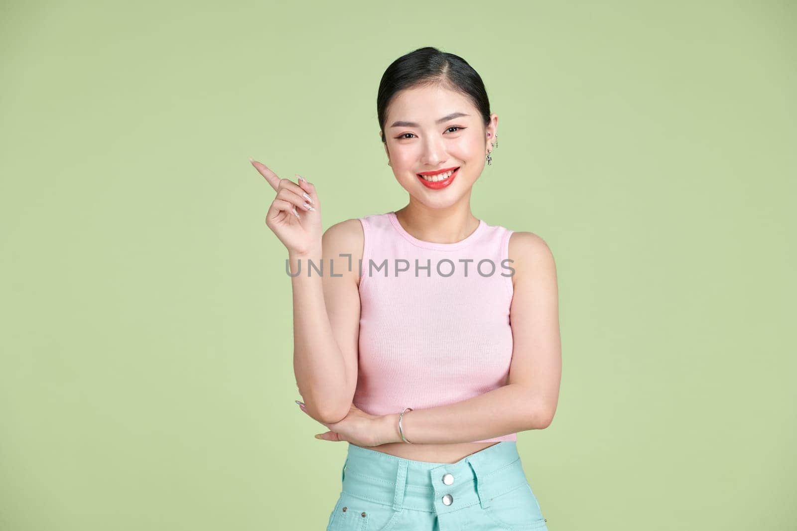 Young elegant beautiful Asian woman smiling and pointing to empty copy space isolated on green background by makidotvn